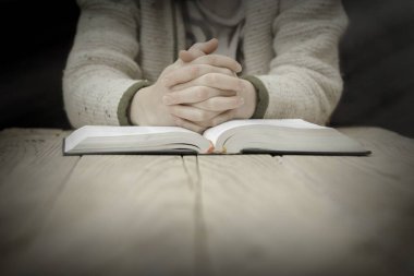 Woman praying over a Bible on a wooden table. (study)