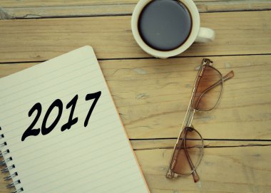 Notebook, specs, cup of coffee on wooden desk (2017)