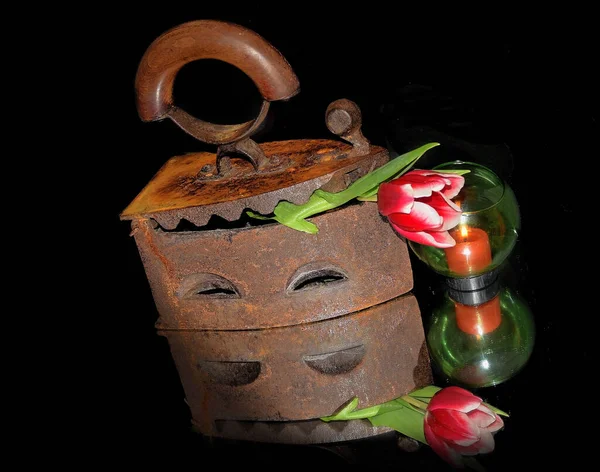 old retro metal iron and flower with candle on dark background, close view