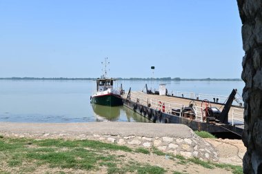 Güneşli bir günde nehir kıyısında demirlemiş teknenin resimli görüntüsü.