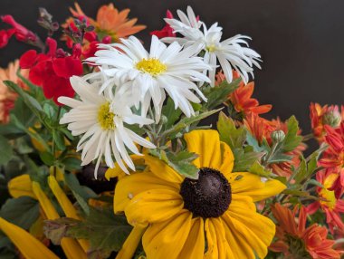 Sarı turuncu beyaz çiçekler ve yeşillik içeren renkli bir buket.