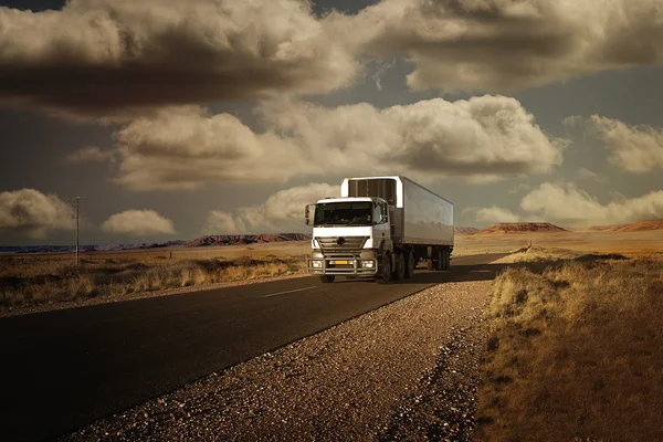 Camion voyageant sur une route dans le désert au coucher du soleil Image En Vente