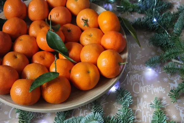 Mandarinen auf einem Teller sind mit einem Weihnachtskranz und nadelgrünen Zweigen verziert — Stockfoto