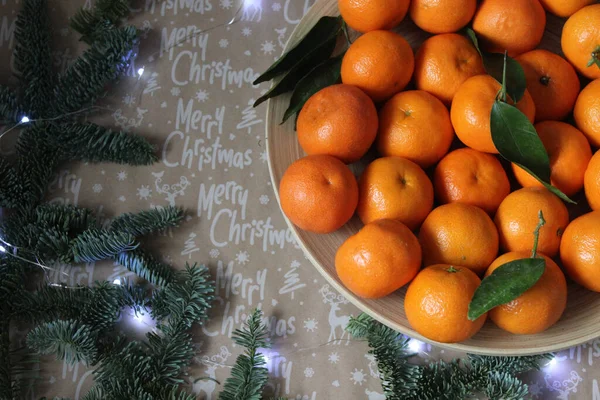 Kleine Mandarinen werden auf einem Teller ausgebreitet und mit einem Weihnachtskranz und nadelgrünen Zweigen verziert. — Stockfoto