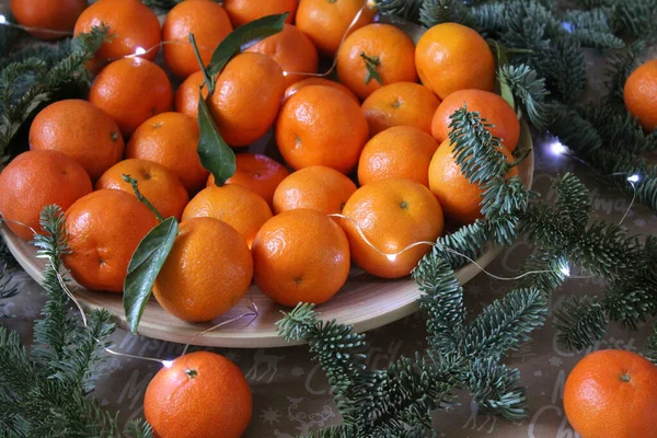 Small tangerines on a plate are decorated with a Christmas garland and coniferous green branches — Stock Photo, Image