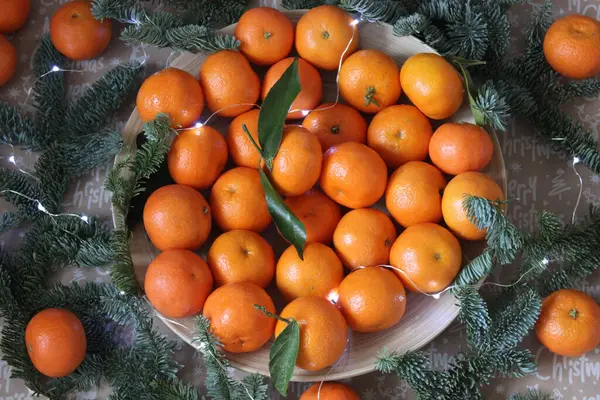 Mandarinen auf einem Teller sind mit Tannenzweigen und einem Weihnachtskranz verziert. Textur oder Hintergrund — Stockfoto