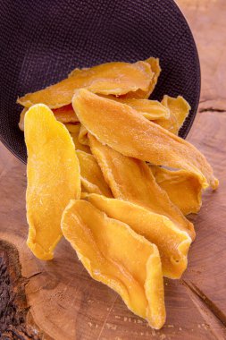 Kurutulmuş mango dilimleri, siyah bir seramik bardaktan dökülüyor.