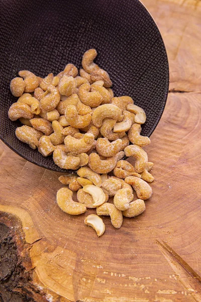 cashew nuts in fine salt spilling out of a dark cup onto a wood