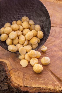 Macadamia çekirdekleri, ahşap bir arka plandaki koyu bir bardaktan düşer..