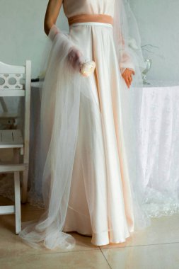 Tüylü pelerinli pembe elbiseli bir kadın beyaz ve pembe bir gül tutuyor.