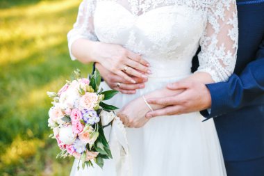 Gelin, ellerinin arasında bir buket tutuyor, damat da beline arkadan sarılıyor.