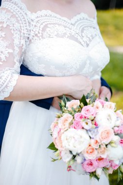 Gelin, ellerinin arasında bir buket tutuyor, damat da beline arkadan sarılıyor.