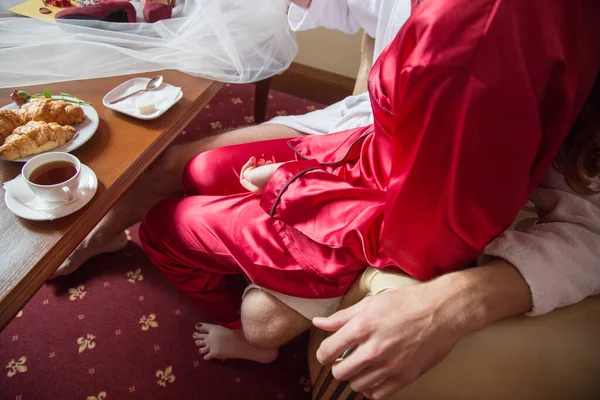 a woman in a red silk robe sits on a man\'s lap