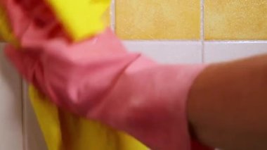 Sarı-beyaz kiremitleri sprey deterjan ve sarı nemli bez ile temizlemek, pembe lastik eldivenli kadın eli