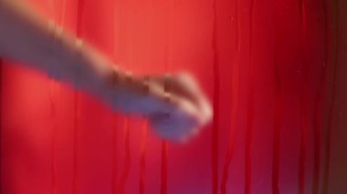 Kadın eli kırmızı arkaplandan ön plandaki ıslak bir bardağa doğru hareket ediyor. Avucunun içinde sarı renkli el yazısı var. Yavaşça elini çek.