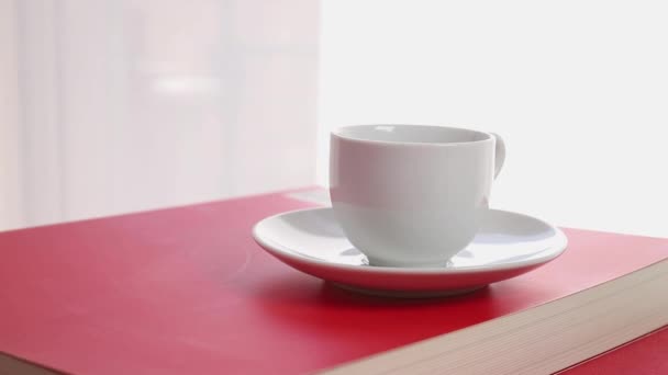 Taza Blanca Café Libro Con Cubierta Roja Fondo Cortinas Blancas — Vídeo de stock