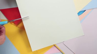 Arka plandaki renkli kağıtlarda, kadın eli makasla renkli kağıt kesiyor 