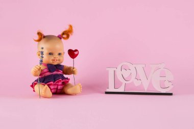 İki kıvırcık kırmızı kuyruklu çilli beyaz kız pembe arka planda üzerinde Aşk yazan bir kalp ve lavanta filizi tutuyor. Yazıtlar ve kartpostallar için yer var. Sevgililer günün kutlu olsun.