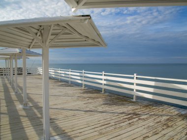 Güneşten gelen mantarlarla dolu beyaz ahşap iskele denizin arka planında ve bulutlu mavi gökyüzü