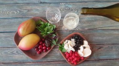 İki toprak kabı - biri mango, kiraz, fesleğen ve nane, diğeri siyah frenk üzümü, mavi peynir, mozarella ve ahududu ile. Kuru beyaz şarapla dolu iki bardak. Ahşap arkaplan