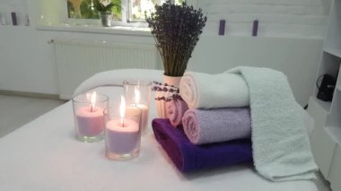 Gevşek balmumlu üç mum, sarılmış lavanta renkli havlular ve masaj salonundaki kanepede çiçek açan bir demet lavanta.