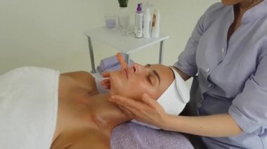 Lavanta renkli takım elbiseli bir kız doktor kanepede uzanan bir kızın yüzüne çok güzel ve profesyonel bir masaj yapar.