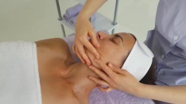 Lavanta renkli takım elbiseli bir kız doktor kanepede uzanan bir kızın yüzüne çok güzel ve profesyonel bir masaj yapar.