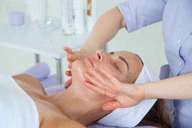 Lavanta renkli takım elbiseli bir kız doktor kanepede uzanan bir kızın yüzüne çok güzel ve profesyonel bir masaj yapar.
