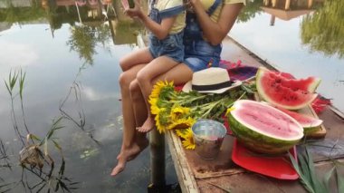 Anne ve dört yaşındaki sarışın kız nehirde bir balık platformunda karpuz yiyorlar.