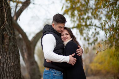 Genç bir adam ve kadın bir sonbahar parkında tatlı tatlı sarılıyorlar.