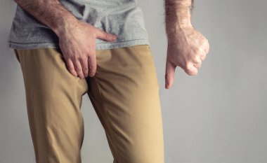 Bej kotlu bir adam cinsel organını ve başparmağını aşağıda tutuyor. Erkekler için hastalık. Cinsel yolla bulaşan enfeksiyonlara karşı korunma kavramı. Testis kanseri.
