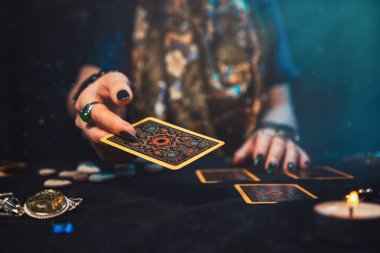 Astroloji ve ezoterizm. Büyücünün kadın eli bir Tarot kartı atıyor. Kapat..