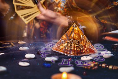 Magic divination and esotericism. Magic glass pyramid with a magical glow. In the background, a fortune teller holds a fan of Tarot cards. Close-up of hands. clipart