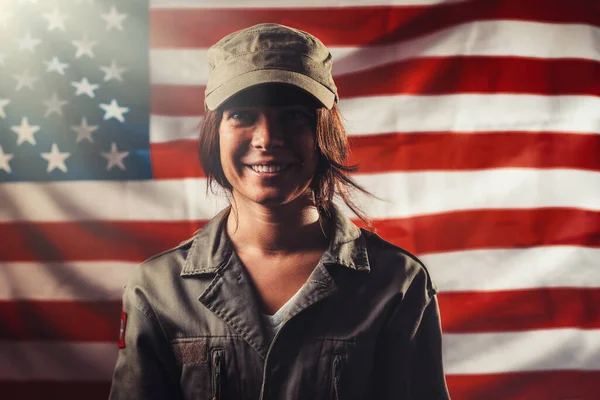 Veterans Day, Memorial Day, Independence Day. Portrait of a smiling female soldier posing against the background of the American flag. Light.