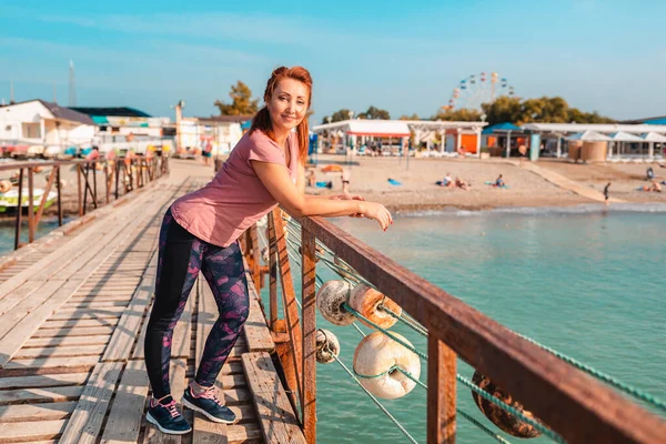 大人の女性スポーツウェアでは 桟橋に立っている サイドビュー 背景のビーチ — ストック写真