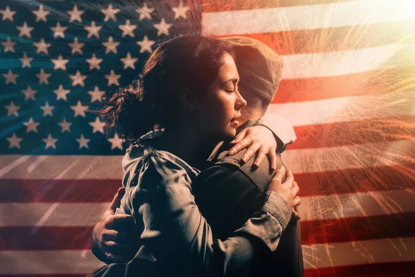 Veterans Day, Memorial Day. A woman embraces a soldier. Couple on the background of the American flag with fireworks. The concept of the American national holidays and patriotism.