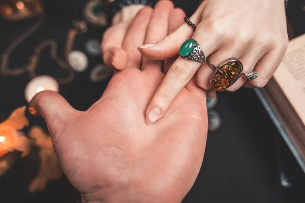 Astroloji ve ezoterizm. Falcı adamın avucunun içini işaret ediyor. Siyah arka planda runikler, bir mum, tılsım ve bir kitap var. Yukarıdan manzara. Eller yukarı..