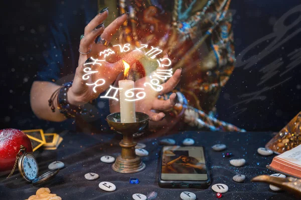 Astroloji ve çevrimiçi kehanet. Bir falcı akıllı telefondan çekilen fotoğraflarla internette falcılık yapıyor. Zodyak çemberi mumun üzerinde resmedilir. Masada sihirli eşyalar var. Eller ve mumlar yakın..