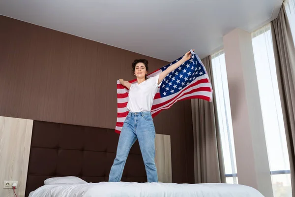 美国的国定假日和爱国主义 一个年轻快乐的女人站在床上挥动着美国国旗 底部视图 — 图库照片