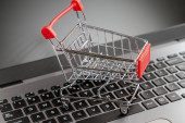 Laptop klávesnice s hračkou nákupní vozík stojí na něm. Zavřít. Rozumím. Koncept online nakupování a moderních technologií.