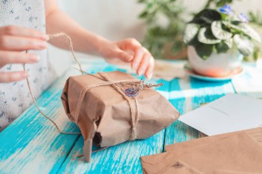 Bir kadın, içi kurumuş çiçeklerle dolu bir paketi el sanatları kağıdına koyar. Eller yakın çekim. Paket alma kavramı.