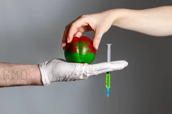 A woman puts a poisoned peach fruit in the hand of a man who holds a syringe with a medicine. The concept of GMO foods, vegetables and fruits.