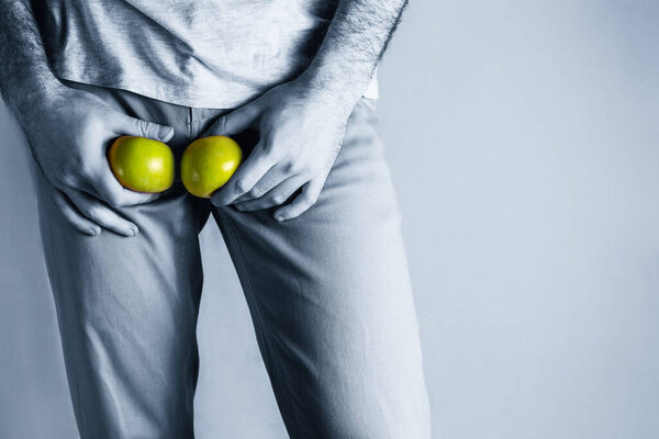 A man in beige jeans at the level of the genitals , holding a ripe and rotten apple. Disease for men. The concept of protection of sexually transmitted infections. Copy space. Blue tint.