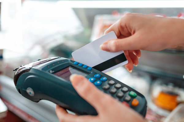 The woman swipes a Bank card through the payment machine to complete the purchase payment. Hands close-up. NFC concept, business and banking operations.