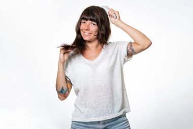 Dövmeli kadın saçlarının uçlarını göstererek gülümsüyor ve saçını tarıyor. Uzayı kopyala Beyaz arka plan. Saç bakımı konsepti.