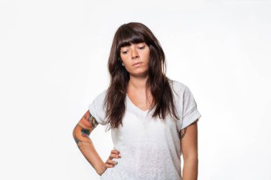 Kolunda dövmesi olan genç, beyaz bir kadın düşünceli bir şekilde poz veriyor, elini yan yatırıyor. Beyaz arka plan. İnsani duygu.