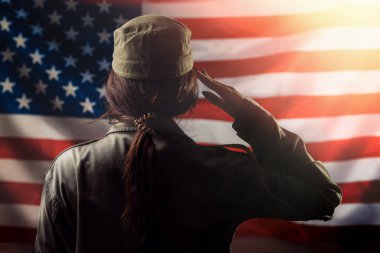Gaziler Günü, Anma Günü, Bağımsızlık Günü. Amerikan bayrağının arka planında selamlaşan bir kadın asker. Arkadan bak. Işık. Ulusal Amerikan bayramı ve vatanseverliği kavramı.