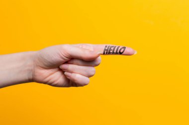 Kadın eli yakın çekim, işaret parmağı mesajı olan bir şeyi işaret ediyor. Yön bulma hareketi. Sarı arka plan. Boşluğu kopyala.