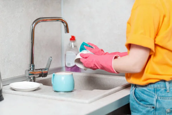 A housewife in casual clothes and pink rubber gloves is washing a cup. Close up of hands.