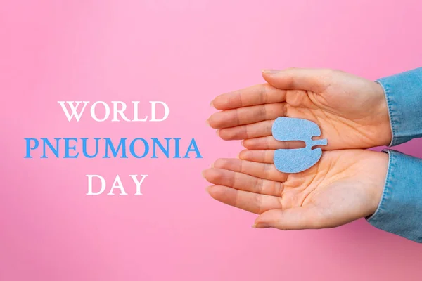 World pneumonia day. Woman\'s hands hold the cut-out silhouette of the lungs. Flat lay. Pink background. Text.